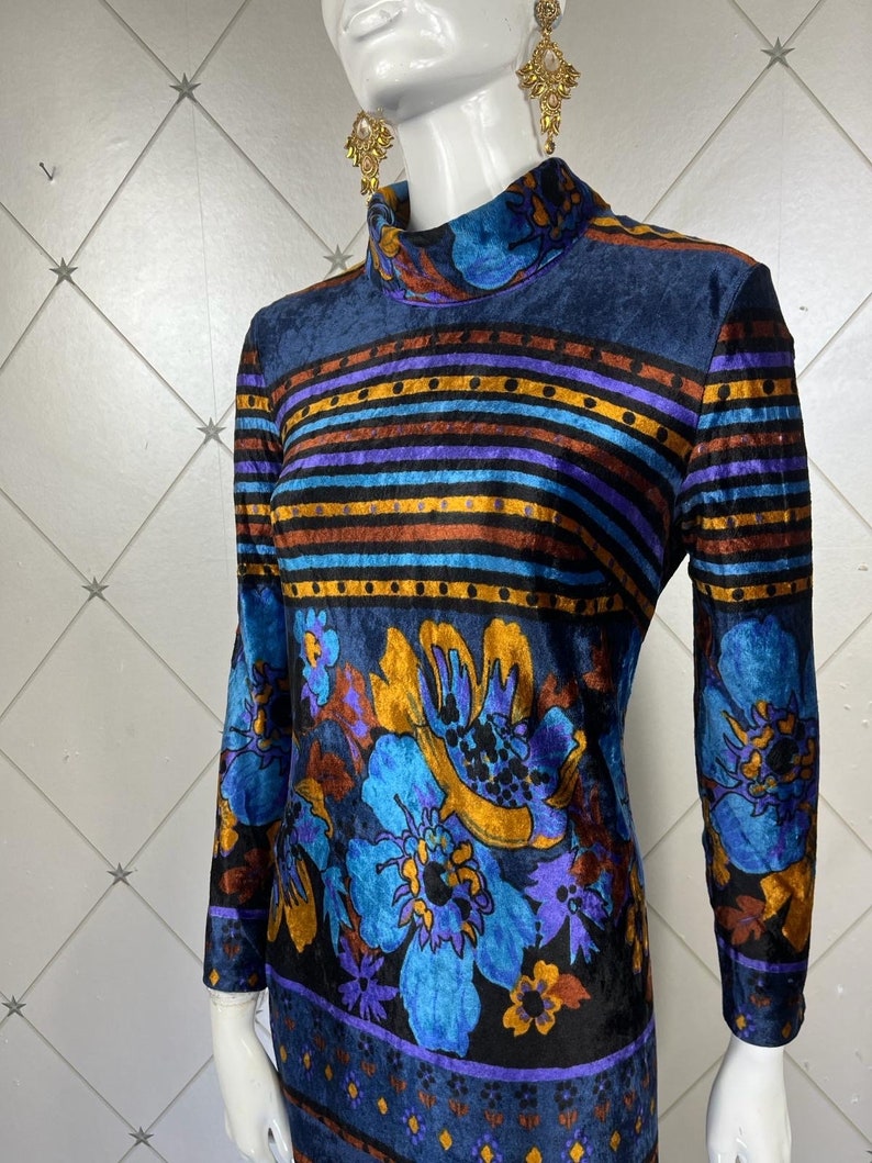 May include: A blue velvet dress with a multi-colored striped pattern and floral print. The dress has a high neck and long sleeves.