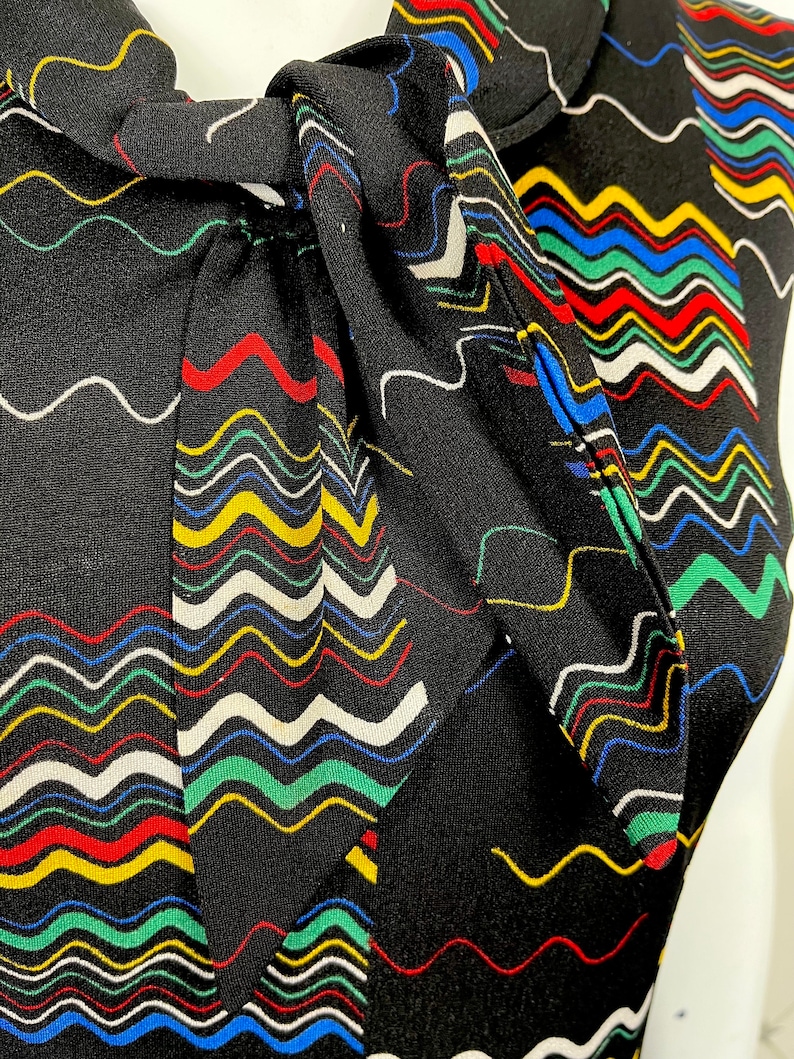 May include: A black sleeveless top with a colorful wavy pattern and a bow tie at the neck.