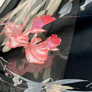 Peut inclure: Tissu noir transparent avec un motif floral de grandes fleurs roses et violettes, et des feuilles grises et beiges. Le tissu est l&eacute;ger, peut-&ecirc;tre une &eacute;charpe ou un v&ecirc;tement.