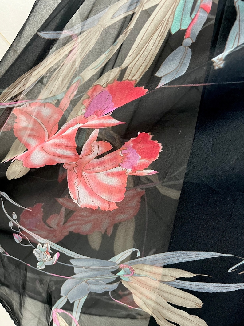 Peut inclure: Tissu noir transparent avec un motif floral de grandes fleurs roses et violettes, et des feuilles grises et beiges. Le tissu est l&eacute;ger, peut-&ecirc;tre une &eacute;charpe ou un v&ecirc;tement.