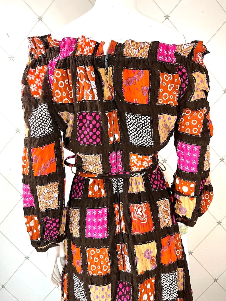 K&ouml;nnte beinhalten: Ein braunes, pinkfarbenes und orangefarbenes Patchworkkleid mit langen &Auml;rmeln und einem quadratischen Ausschnitt. Das Kleid hat einen Rei&szlig;verschluss auf der R&uuml;ckseite und einen G&uuml;rtel.