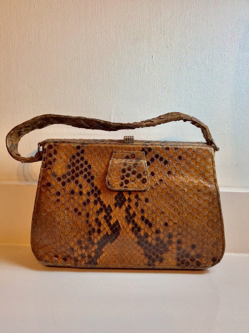 May include: A vintage brown snakeskin handbag with a clasp closure and a short strap.