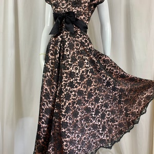 May include: A black lace dress with a sweetheart neckline and a black satin bow at the waist. The dress has a full skirt and is made of a delicate lace fabric.