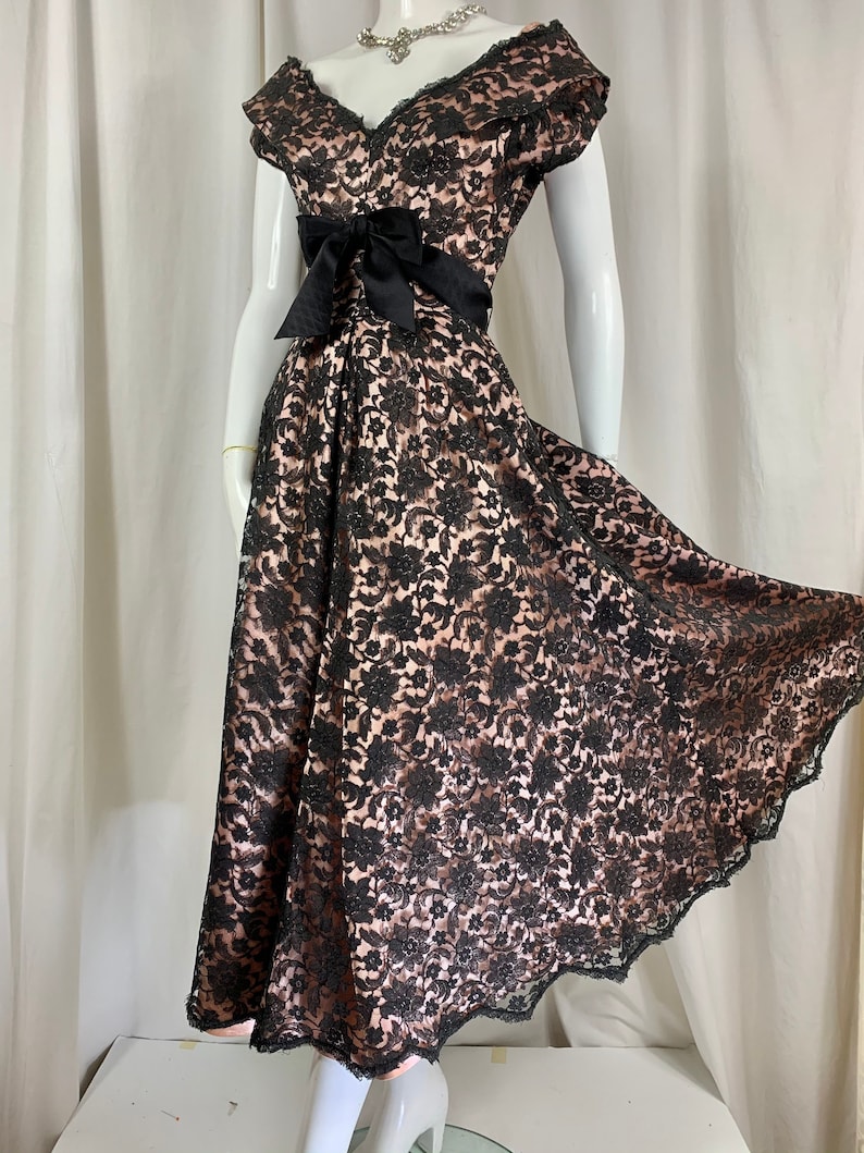 May include: A black lace dress with a sweetheart neckline and a black satin bow at the waist. The dress has a full skirt and is made of a delicate lace fabric.