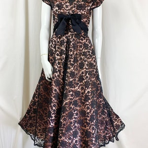 May include: A black lace dress with a sweetheart neckline and a black satin bow at the waist. The dress has a full skirt and is made of a sheer fabric.