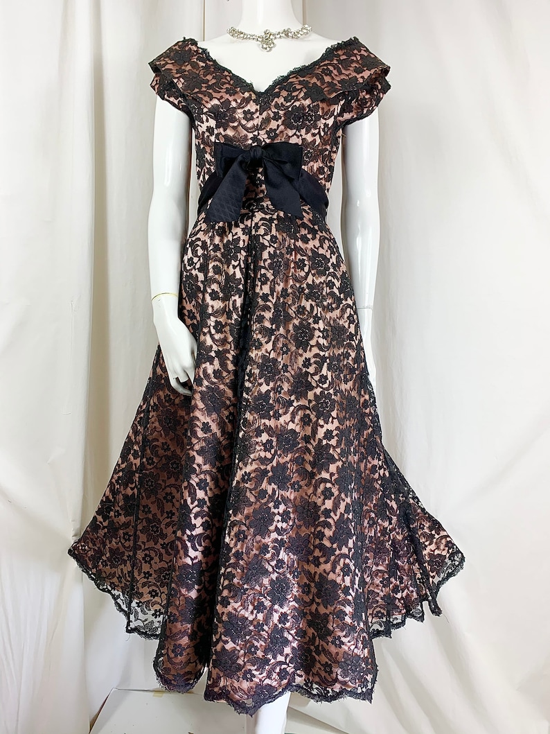 May include: A black lace dress with a sweetheart neckline and a black satin bow at the waist. The dress has a full skirt and is made of a sheer fabric.