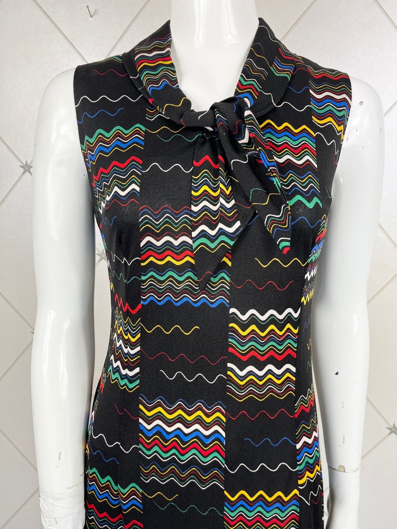 May include: A sleeveless dress with a black background and a colorful wavy pattern. The dress has a tie at the neck.