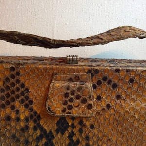 May include: A vintage snakeskin clutch purse with a brown and black pattern. The purse has a metal clasp and a flap with a small pocket.