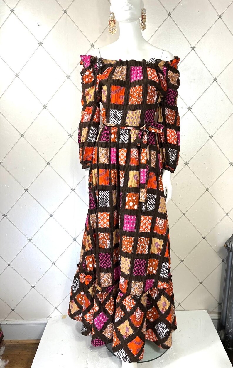 K&ouml;nnte beinhalten: Ein langes, schulterfreies Kleid mit Patchwork-Muster in Braun-, Orange-, Rosa- und Wei&szlig;t&ouml;nen. Das Kleid hat einen figurbetonten Oberteil und einen flie&szlig;enden Rock mit einem R&uuml;schen-Saum.