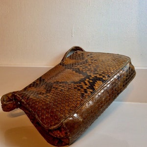 May include: A brown snakeskin clutch purse with a flap closure and a short strap.