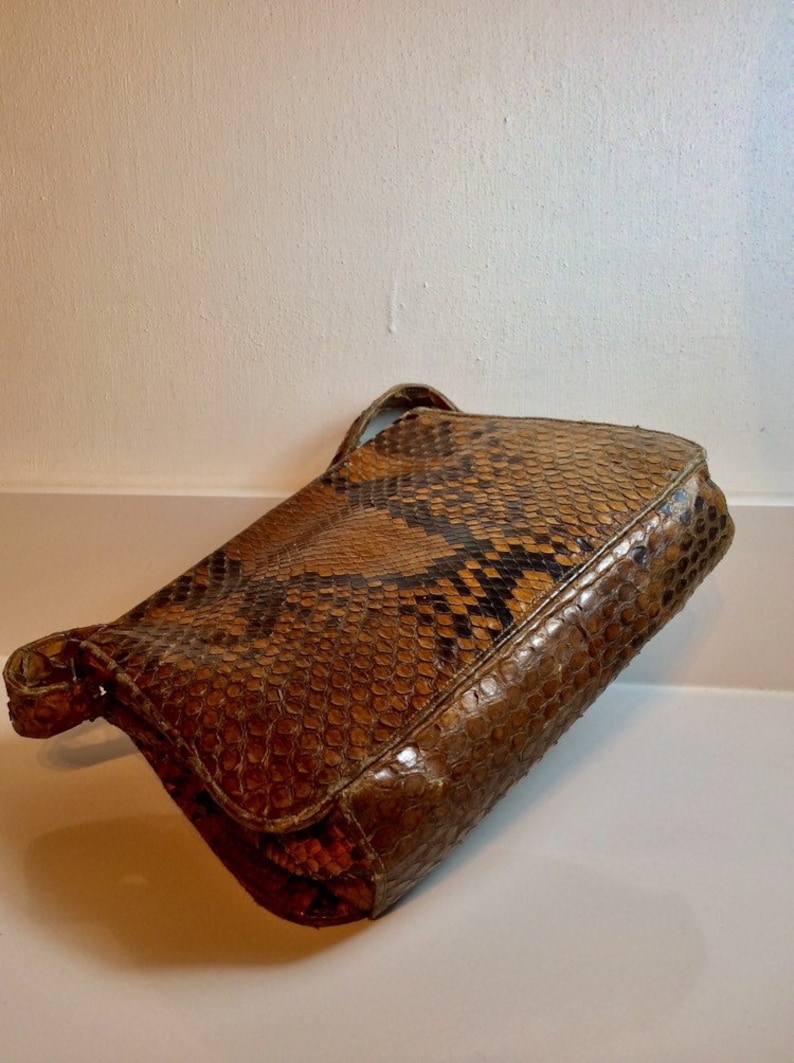 May include: A brown snakeskin clutch purse with a flap closure and a short strap.
