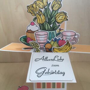 Tarjeta de cumpleaños, mesa puesta con ramo de flores y frutas.