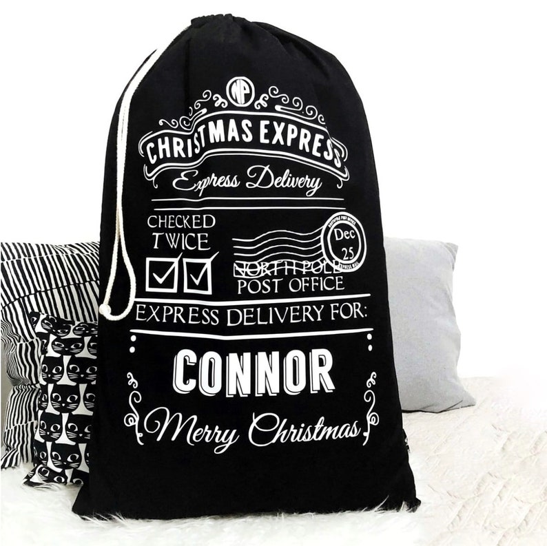 Op de afbeelding: Zwarte kerstcadeauzak met witte tekst. De tekst luidt "CHRISTMAS EXPRESS Express Delivery" en "CONNOR Merry Christmas". Voorzien van een trekkoord en feestelijke afbeeldingen.
