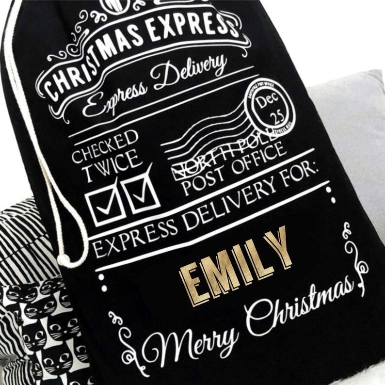 Op de afbeelding: Zwarte kerstcadeauzak met witte tekst "CHRISTMAS EXPRESS" en "Express Delivery". De tas heeft een trekkoordsluiting en bevat de naam "EMILY" in gouden letters. De tas zegt ook "Merry Christmas".