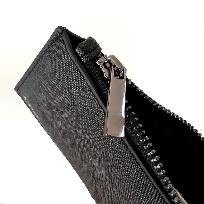 K&ouml;nnte beinhalten: Eine schwarze Rei&szlig;verschlusstasche mit einem silbernen Rei&szlig;verschluss. Die Tasche ist aus einem strukturierten Material.