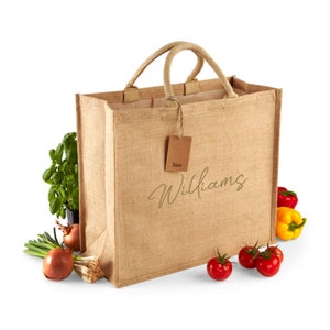 Puede incluir: Una bolsa de yute marrón con la palabra "Williams" impresa en la parte delantera. La bolsa está llena de productos frescos, incluyendo tomates, cebollas y pimientos.