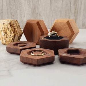 May include: Six hexagonal wooden ring boxes, three are made of dark wood and three are made of light wood. The dark wood boxes have a velvet interior and are designed to hold rings. The light wood boxes are decorative and have a natural wood finish.
