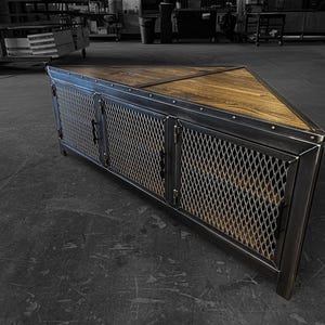 以下が含まれることがあります： 3 つの金属製のドアと木製の天板が付いた三角形のインダストリアルスタイルのメディアコンソール。ドアはワイヤーメッシュのデザインで、金属のリベットでアクセントが付けられています。