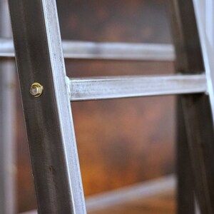 May include: Close-up of a metal shelf unit with a brass screw. The shelf unit is made of black metal with a brushed finish.