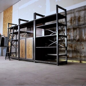 May include: A large, industrial-style shelving unit with a ladder, wooden doors, and metal shelves. The unit is made of black metal and has a rustic, industrial look.