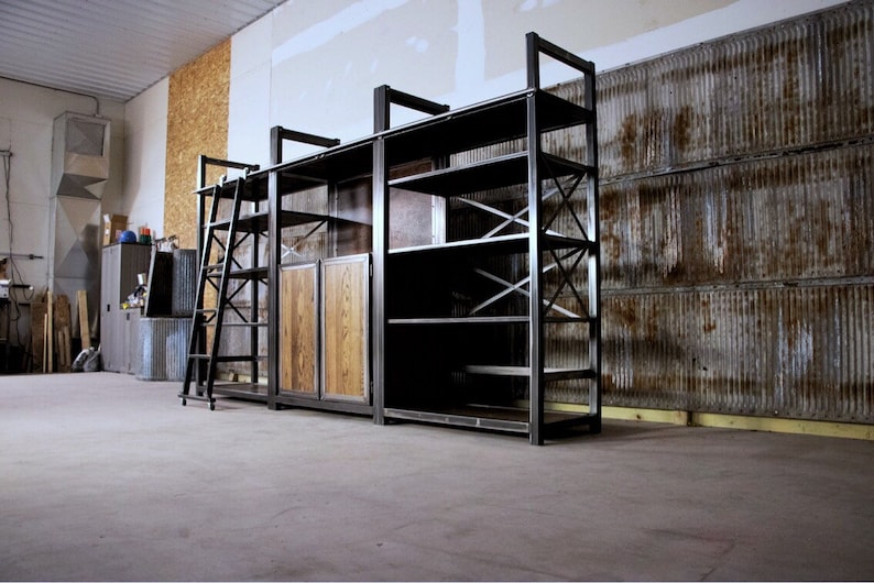 May include: A large, industrial-style shelving unit with a ladder, wooden doors, and metal shelves. The unit is made of black metal and has a rustic, industrial look.