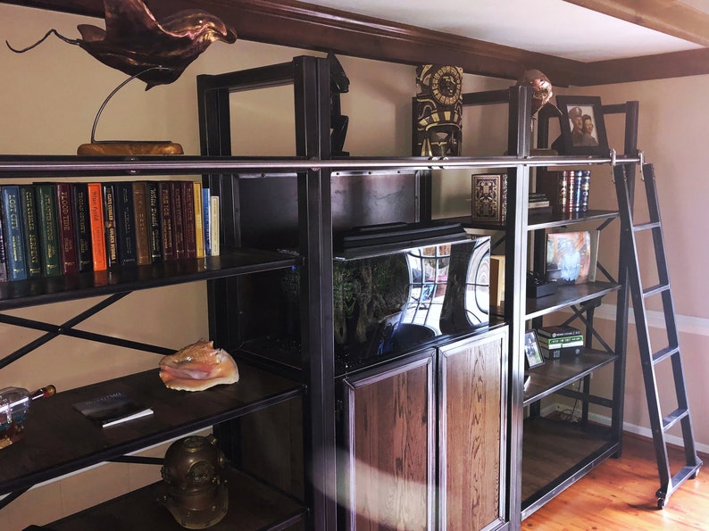 May include: A black metal bookshelf unit with a ladder, featuring a fish tank, books, and decorative items. The shelves are made of wood and metal.