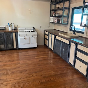 Puede incluir: Una estufa vintage blanca con una puerta de horno negra y detalles cromados se encuentra en una cocina con pisos de madera y gabinetes de madera oscura con detalles met&aacute;licos. Los gabinetes tienen un dise&ntilde;o de malla met&aacute;lica en las puertas.