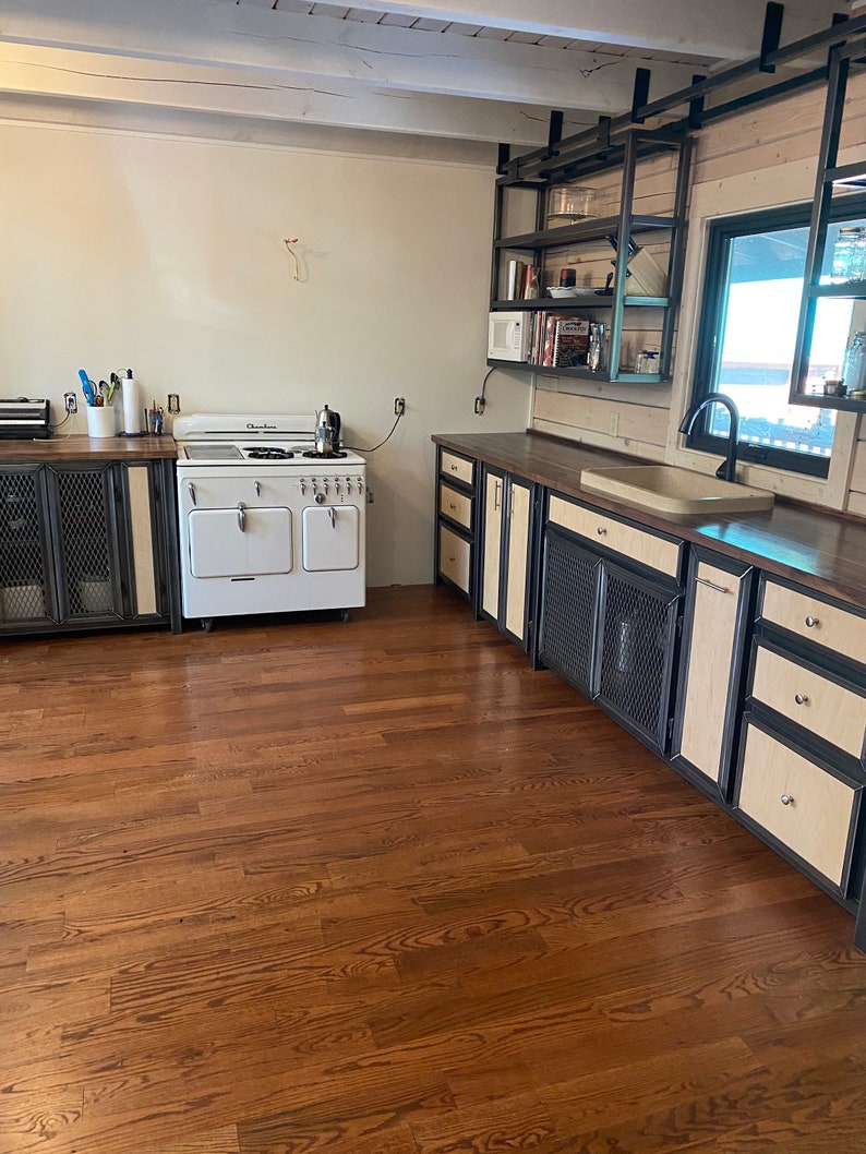 Puede incluir: Una estufa vintage blanca con una puerta de horno negra y detalles cromados se encuentra en una cocina con pisos de madera y gabinetes de madera oscura con detalles met&aacute;licos. Los gabinetes tienen un dise&ntilde;o de malla met&aacute;lica en las puertas.