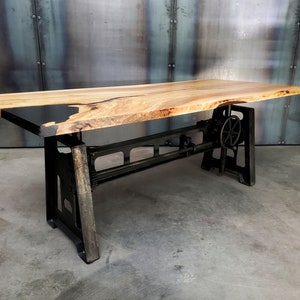 May include: A wooden table top with black epoxy resin inlay, supported by a black metal adjustable base with a hand crank.