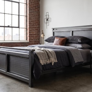 May include: A dark metal bed frame featuring a textured diamond-patterned headboard and footboard. The bed is dressed with dark grey bedding, a light-coloured throw blanket, and a brown leather accent pillow, paired with a matching metal nightstand.