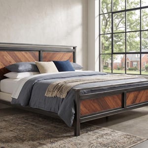 May include: A bed frame constructed from dark metal with rectangular headboard and footboard panels featuring a brown wood grain in a chevron pattern. The bed is dressed with a grey duvet, a beige throw blanket, and three pillows in grey, beige, and navy blue.