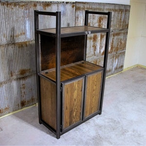 Op de afbeelding: Een houten kast met twee deuren en twee planken, gemaakt van metaal en hout. De kast heeft een rustieke industriële stijl.