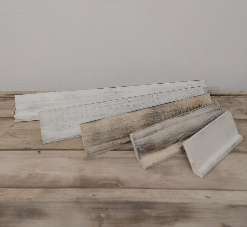 May include: Five wooden signs of varying sizes, all painted white with a distressed finish. The signs are arranged in a staggered pattern on a wooden surface.