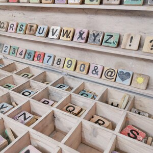 May include: A wooden box with compartments filled with colorful letter tiles and number tiles. The tiles are made of wood and have a distressed look. The box is a great way to store and organize letter tiles for games or crafts.