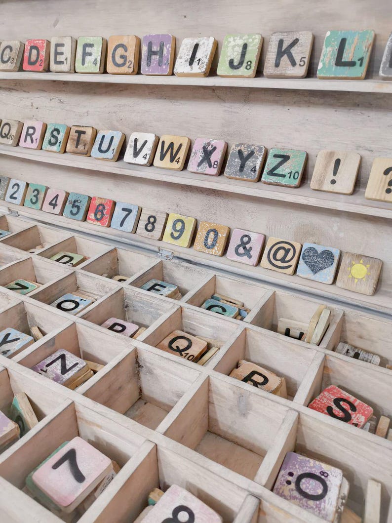 May include: A wooden box with compartments filled with colorful letter tiles and number tiles. The tiles are made of wood and have a distressed look. The box is a great way to store and organize letter tiles for games or crafts.