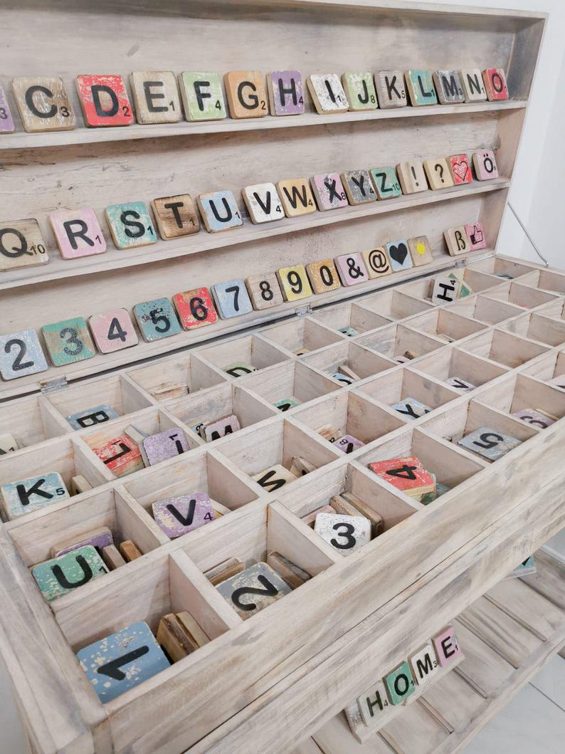 May include: A wooden box with a whitewashed finish, containing a collection of vintage letter tiles. The tiles are arranged in alphabetical order and include numbers, punctuation marks, and symbols. The box has a two-tiered design, with the top tier containing the letters and the bottom tier containing the numbers and symbols.