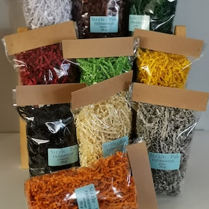 Könnte beinhalten: Verschiedene farbige Papier-Füllmaterialien in transparenten Plastiktüten. Farben: Weiß, Braun, Grün, Gelb, Rot, Schwarz, Beige, Grau und Orange. Jede Tüte hat ein blaues Etikett mit der Aufschrift "Sizzle-Pak Füllmaterial (50 g)".