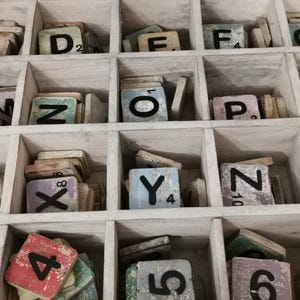 May include: A wooden box with compartments filled with letter tiles. The tiles are made of wood and have black letters on them. The box is painted white and has a distressed look. The tiles are arranged in alphabetical order.