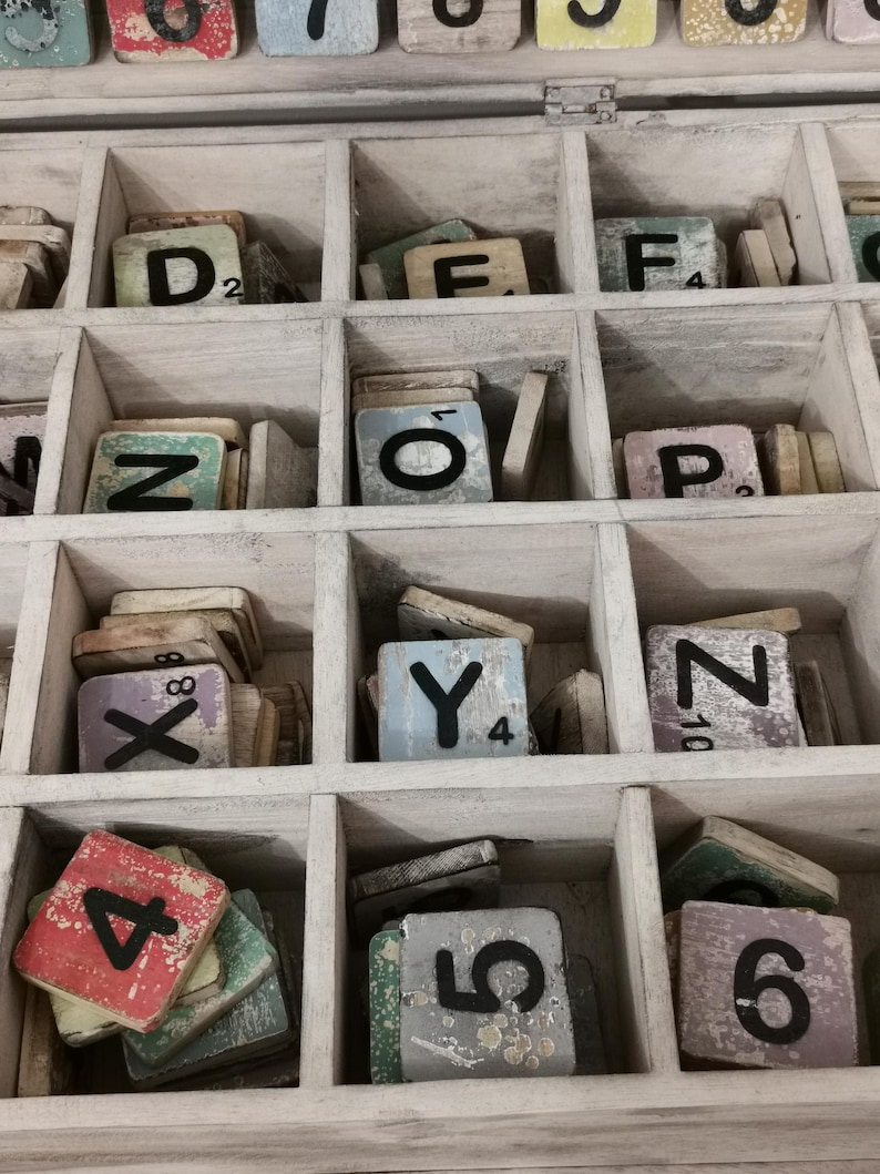 May include: A wooden box with compartments filled with letter tiles. The tiles are made of wood and have black letters on them. The box is painted white and has a distressed look. The tiles are arranged in alphabetical order.