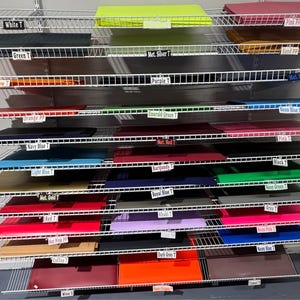 Puede incluir: Una estantería de alambre de varios niveles que muestra numerosas pilas de láminas planas y rectangulares en varios colores. Cada pila está etiquetada con pequeñas etiquetas en blanco y negro que identifican colores como blanco, amarillo neón, rosa, verde, plata metálico, arena, amarillo, morado, azul metálico, naranja, verde esmeralda, azul neón, azul marino, rojo metálico, azul claro, burdeos, negro, oro metálico, azul real, verde neón, rojo, caqui, gris, rosa fuerte, lila, rosa neón, café, gris oscuro, azul neón, vino, naranja neón y camel.