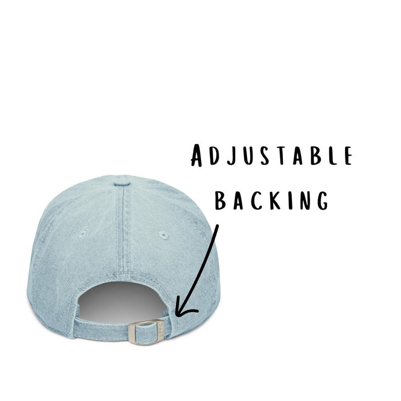 May include: A light blue denim baseball cap featuring a silver-toned metal buckle closure at the back. The text ADJUSTABLE BACKING is printed in black above an arrow pointing to the metal buckle, highlighting the adjustable strap feature.