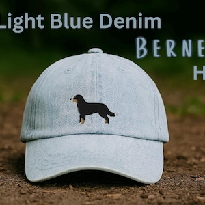 May include: A light blue denim baseball cap featuring an embroidered Bernese Mountain Dog on the front panel. The text Light Blue Denim BERNER Hat is printed in the upper portion of the frame. The cap has a curved brim and a structured crown.