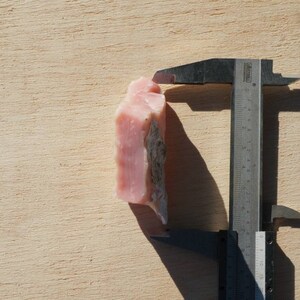 Pode incluir: Uma pedra bruta de opala rosa sendo medida com um paqu&iacute;metro. A pedra tem aproximadamente 3,5 cent&iacute;metros de altura.