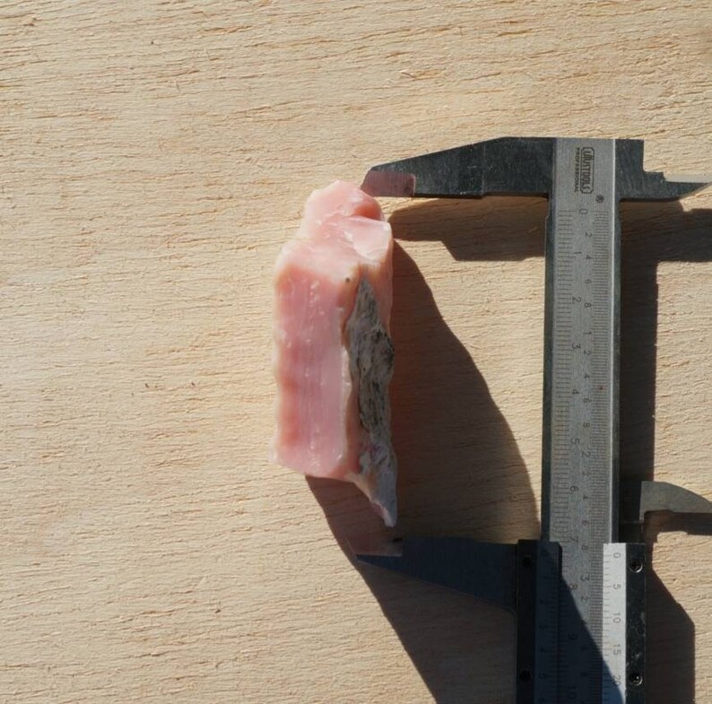 Pode incluir: Uma pedra bruta de opala rosa sendo medida com um paqu&iacute;metro. A pedra tem aproximadamente 3,5 cent&iacute;metros de altura.
