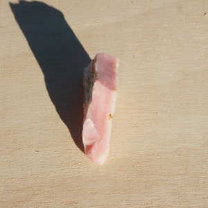 Pode incluir: Um cristal de opala rosa com uma textura &aacute;spera e natural. O cristal &eacute; transl&uacute;cido e tem uma tonalidade rosa claro.