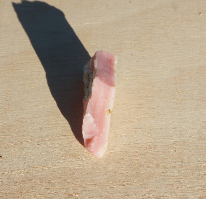 Pode incluir: Um cristal de opala rosa com uma textura &aacute;spera e natural. O cristal &eacute; transl&uacute;cido e tem uma tonalidade rosa claro.