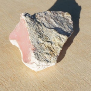 Op de afbeelding: Een ruwe, roze en witte opaal steen met een natuurlijke, onregelmatige vorm.
