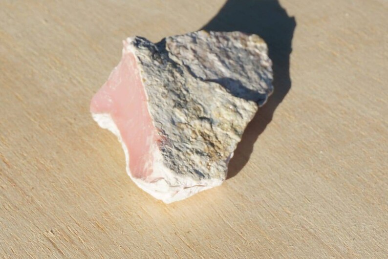 Op de afbeelding: Een ruwe, roze en witte opaal steen met een natuurlijke, onregelmatige vorm.