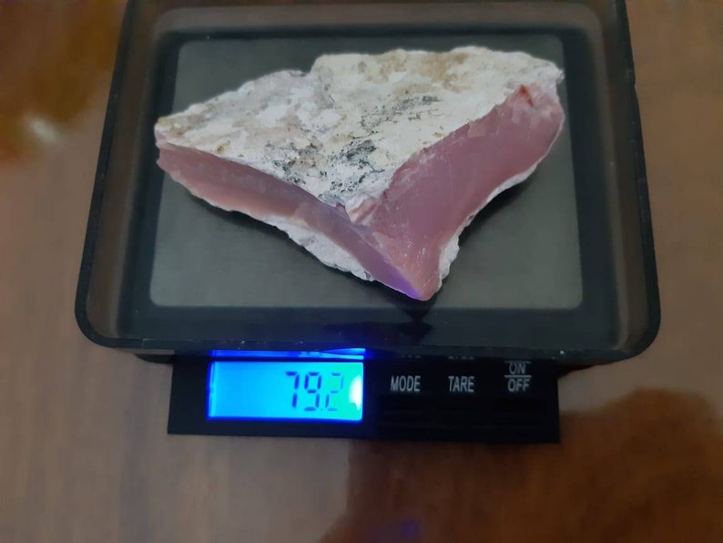 Op de afbeelding: Een roze en witte opaal steen op een digitale weegschaal. De weegschaal geeft 7,92 aan.