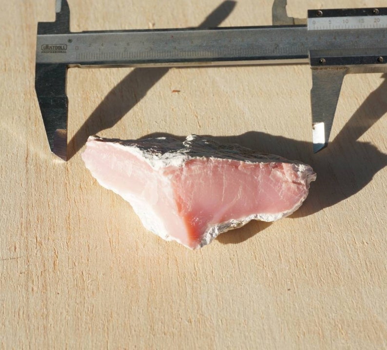Op de afbeelding: Een roze en grijze agaat steen met een ruwe, natuurlijke textuur. De steen wordt gemeten met een schuifmaat, om de grootte te laten zien.